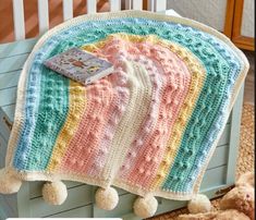 a crocheted blanket with pom poms on it and a book laying on top