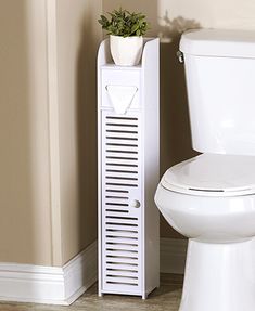 a white toilet sitting next to a small plant on top of a wooden cabinet in a bathroom