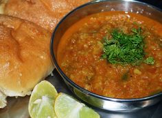 a bowl of soup with bread and limes on the side for garnish