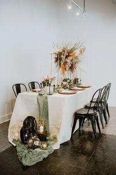 the table is set with black chairs and white linens, greenery on top