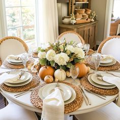 a dining room table set for thanksgiving with pumpkins and white flowers in the center