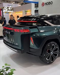 the rear end of a green suv on display at an auto show with people standing around