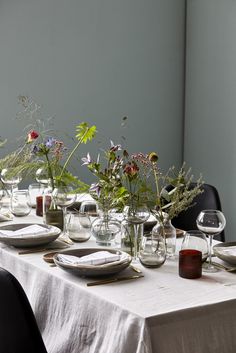 the table is set with plates and vases filled with wildflowers in clear glassware