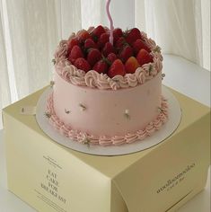 a pink birthday cake with strawberries on top and a lit candle in the middle