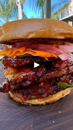 a large sandwich with meat, cheese and onions on a wooden table in front of palm trees