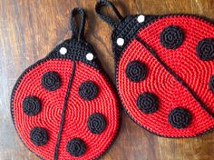 two crocheted ladybugs are sitting on a wooden table together, one is red and the other is black