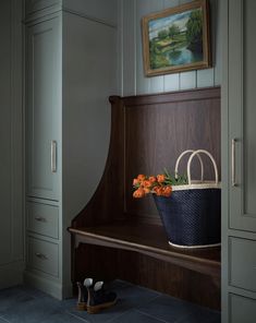 a basket with flowers sitting on top of a wooden bench next to a painting hanging above it