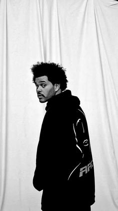 a black and white photo of a young man in front of a white backdrop wearing a hoodie