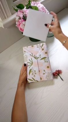 two hands holding open boxes on top of a table with pink flowers in the background