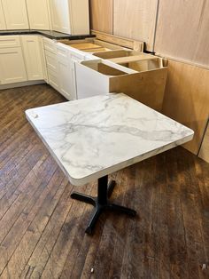 an empty kitchen with white cabinets and marble top table in the foreground, on wooden flooring