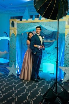 a man and woman pose for a photo in front of a backdrop with an umbrella