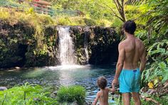 a man and his child are standing in front of a waterfall while looking at the water