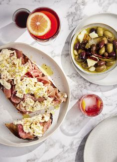 a table topped with plates and bowls filled with different types of food next to glasses of wine