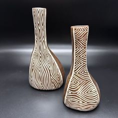 two vases sitting next to each other on a black surface with white and brown designs