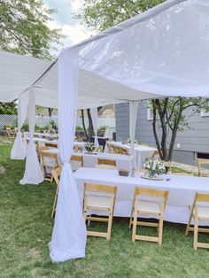 tables and chairs are set up under a white canopy for an outdoor wedding reception in the grass