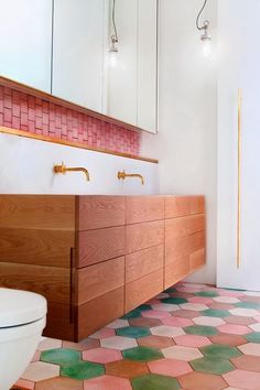 a white toilet sitting next to a wooden vanity in a bathroom under a mirror with pink and green tiles on the floor