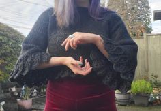 a woman with purple hair wearing a black sweater and red velvet skirt holding her hands together