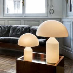 two lamps sitting on top of a table next to a black couch in a living room