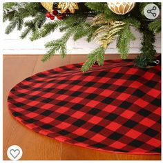 a red and black plaid christmas tree skirt on top of a wooden floor next to a potted plant