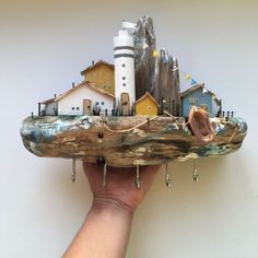 a hand holding a piece of wood with houses on it and a lighthouse in the background