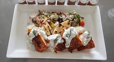 a white plate topped with meat and veggies next to bottles of ketchup