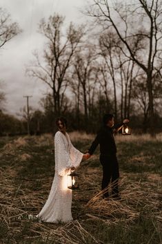 a bride and groom holding hands in a field at night with lanterns lit up on the ground