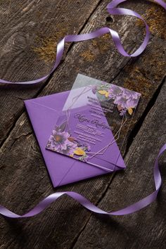 a purple and white wedding card on top of a wooden table next to a ribbon