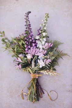 a bunch of purple and white flowers tied to a string on the ground with some green leaves