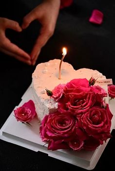 a heart shaped cake with pink roses on it and someone holding the candle in the shape of a heart