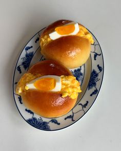 two hot dogs with eggs on them sitting on a blue and white plate next to each other