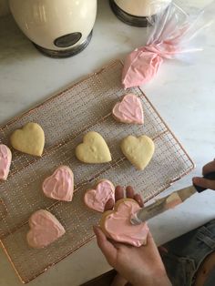 someone is decorating heart shaped cookies with pink icing on a wire cooling rack