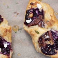 two pastries with blueberries and other toppings sitting on a piece of parchment paper