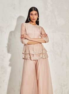 Editor's Note Blush scallop flora peplum and sharara is an elegant ethnic wear set, made of lightweight organza fabric. The peplum top features a beautiful floral embellishment and a scallop hemline. The set includes a pair of sharara pants with a flared silhouette. Color: Blush Fabric: Organza Component: Peplum and sharara Occasion: Cocktail and wedding guest Embroidery: Floral hand & machine embellishment Disclaimer: Product color may slightly vary due to photographic lighting sources or your Elegant Floral Embroidered Pant Set For Diwali, Ruffled Dresses For Eid Reception, Eid Reception Dress With Ruffles, Elegant Peplum Set In Georgette, Elegant Georgette Peplum Set, Organza Palazzo Set With Floral Embroidery For Party, Elegant Peplum Palazzo Set With Resham Embroidery, Wedding Pant Set With Sheer Dupatta In Georgette, Elegant Resham Embroidered Peplum Palazzo Set