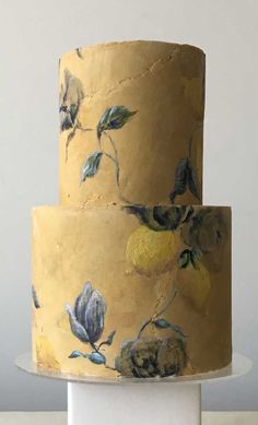 a three tiered cake with yellow and blue flowers on the top, sitting on a white pedestal