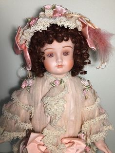 an antique doll is wearing a pink dress and bonnet with feathers on it's head