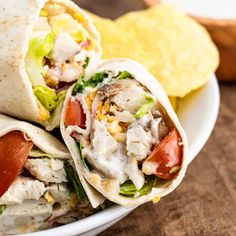 two wraps filled with chicken, lettuce and tomato on a plate next to chips