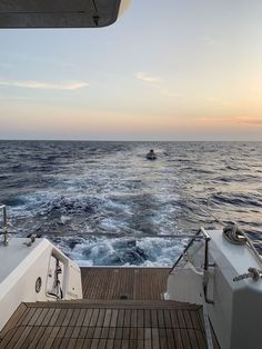 a boat traveling through the ocean at sunset with another boat in the water behind it