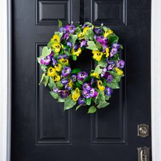 a wreath with purple and yellow pansies hangs on the front door's black door