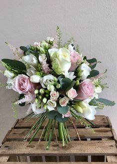 a bouquet of white and pink flowers sitting on top of a wooden crate with greenery