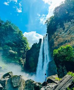 a person standing on rocks in front of a waterfall with water pouring from the top