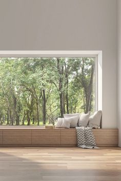 a window seat with pillows on it in front of a wooden floor and large windows