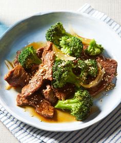 a white plate topped with beef and broccoli on top of a blue table cloth