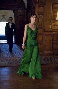 a woman in a green dress is standing on the floor with her hands behind her back