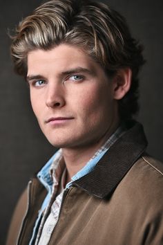 a man with blonde hair and blue eyes is posing for a studio photo in front of a black background