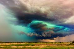 the sky is filled with green and blue clouds as it moves through an open field