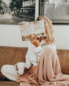 a person sitting on a couch reading a book and holding a coffee cup in front of their face