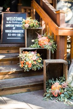 flowers and greenery are arranged on the steps at an outdoor wedding venue in front of a welcome sign