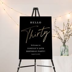 a black and gold birthday party sign sitting on top of a easel next to a vase filled with flowers