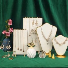 a collection of jewelry sitting on top of a green cloth covered table next to a vase filled with pink roses