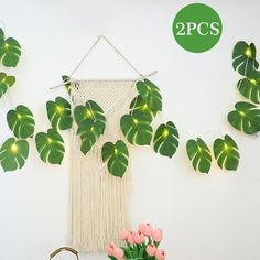 there is a wall hanging with green leaves on it and pink flowers in the vase